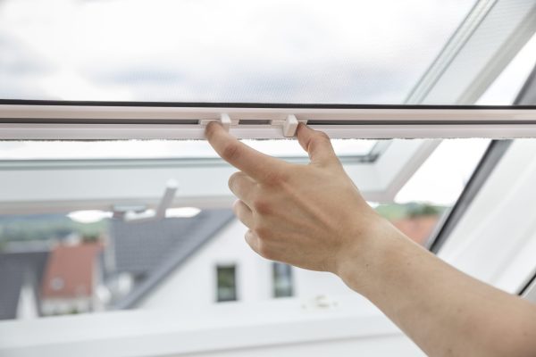 Insektenschutzrollo für Dachfenster, Hand bedient den Griff am Fliegengitterrollo