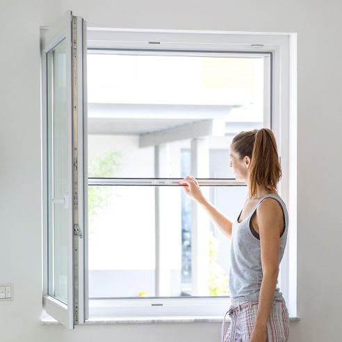 Rollo für Fenster mit Insektenschutz, Frau bedient das Rollo am geöffneten Fenster