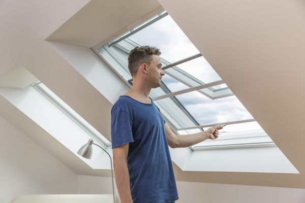 Insektenschutzrollo für Dachfenster, Mann lüftet am geöffneten Dachfenster im Dachgeschoss