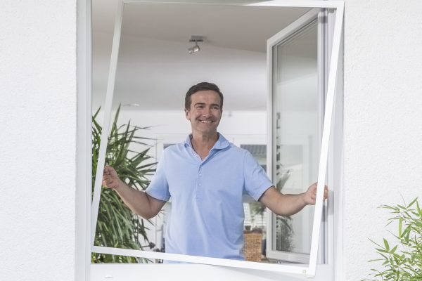 Insektenschutz Spannrahmen am Fenster, Mann öffnet den Spannrahmen