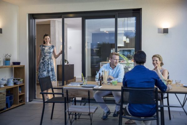 Insektenschutz Schiebetür an großer Terrassenfront, Freunde sitzen gemeinsam am Tisch bei geöffneter Tür
