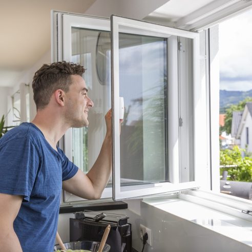 Insektenschutz für Dreh- und Pendelfenster, Mann öffnet das Fenster in der Küche und lüftet ohne Insekten