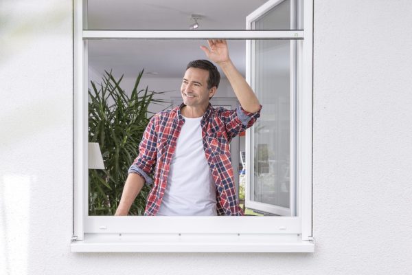 Insektenschutzrollo für Fenster, Mann bedient das Rollo am geöffneten Fenster